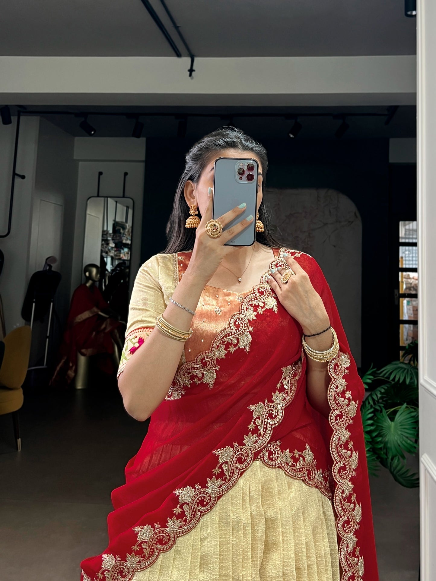 Woman in a red and gold saree taking a mirror selfie in a room.