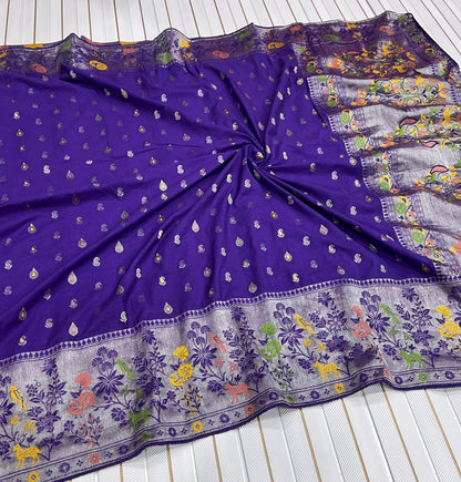 A purple Banarasi silk saree or fabric piece with small metallic motifs and a heavily embroidered floral border, laid flat on a white slatted surface.