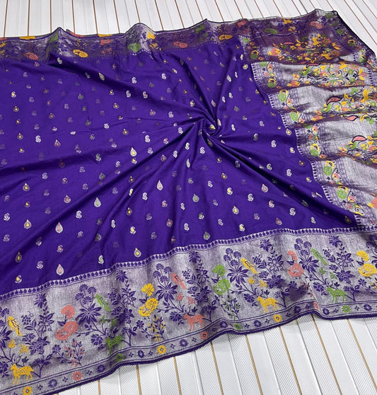 A purple Banarasi silk saree or fabric piece with small metallic motifs and a heavily embroidered floral border, laid flat on a white slatted surface.